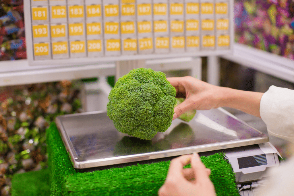 Balance fruits et légumes avec une main de femme déposant un brocolis 