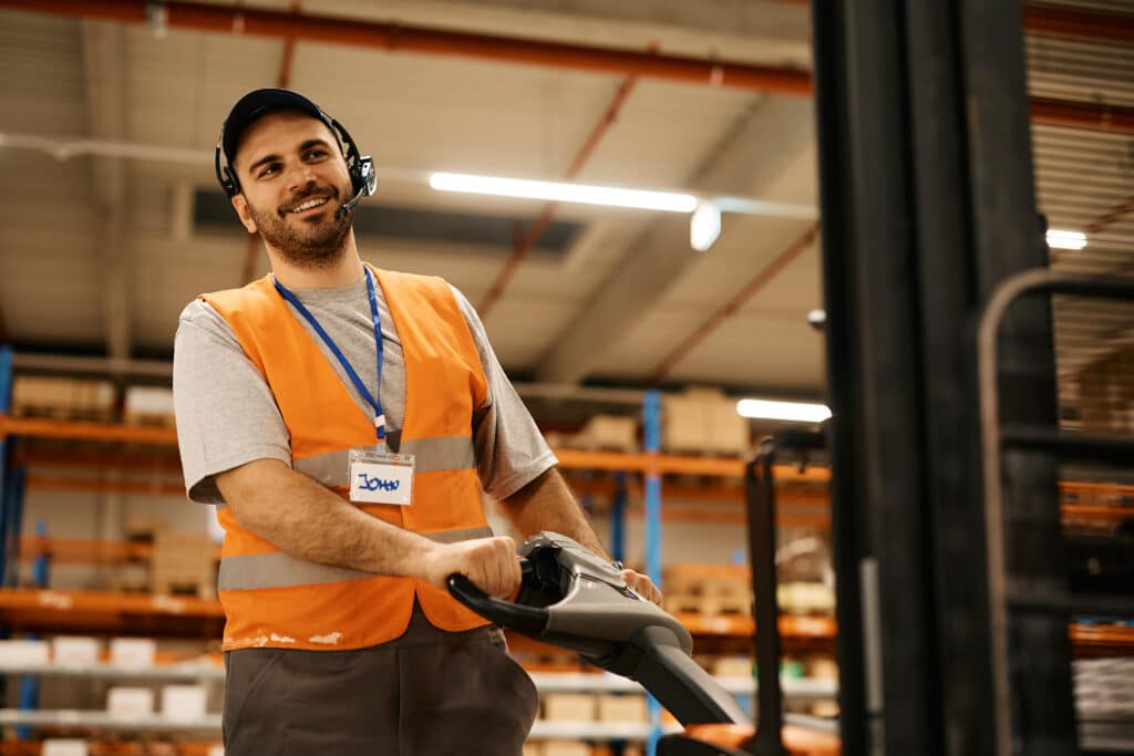 Heureux travailleur masculin utilisant un transpalette tout en travaillant dans un entrepôt de distribution.