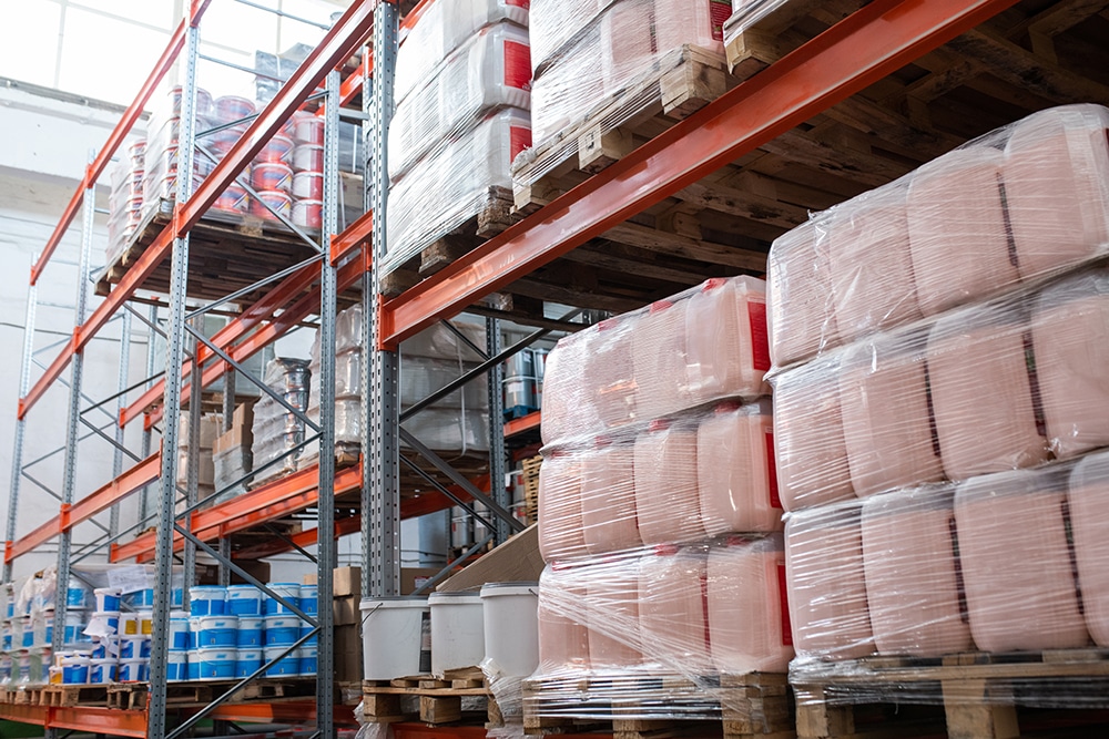 Bidons recouverts de film étirable placés sur des palettes dans la salle de stockage, cadre métallique avec articles